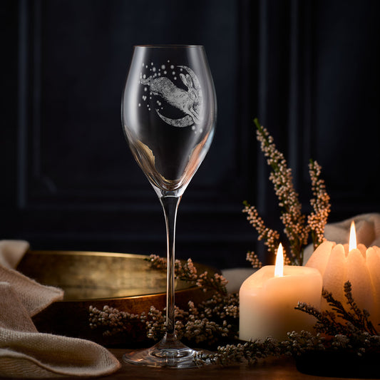 Prosecco glass with engraved winter hare and crescent moon design on a table with candles and flowers