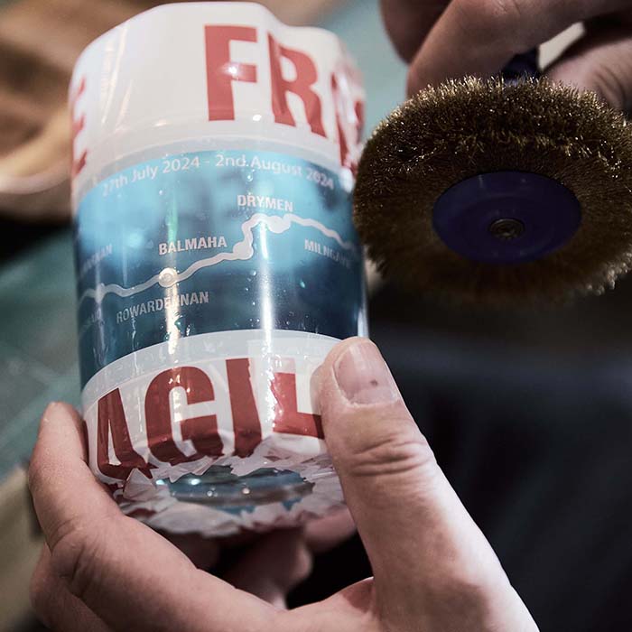 Person holding a cylindrical container with text and graphics, next to a brush with a metallic bristle head.
