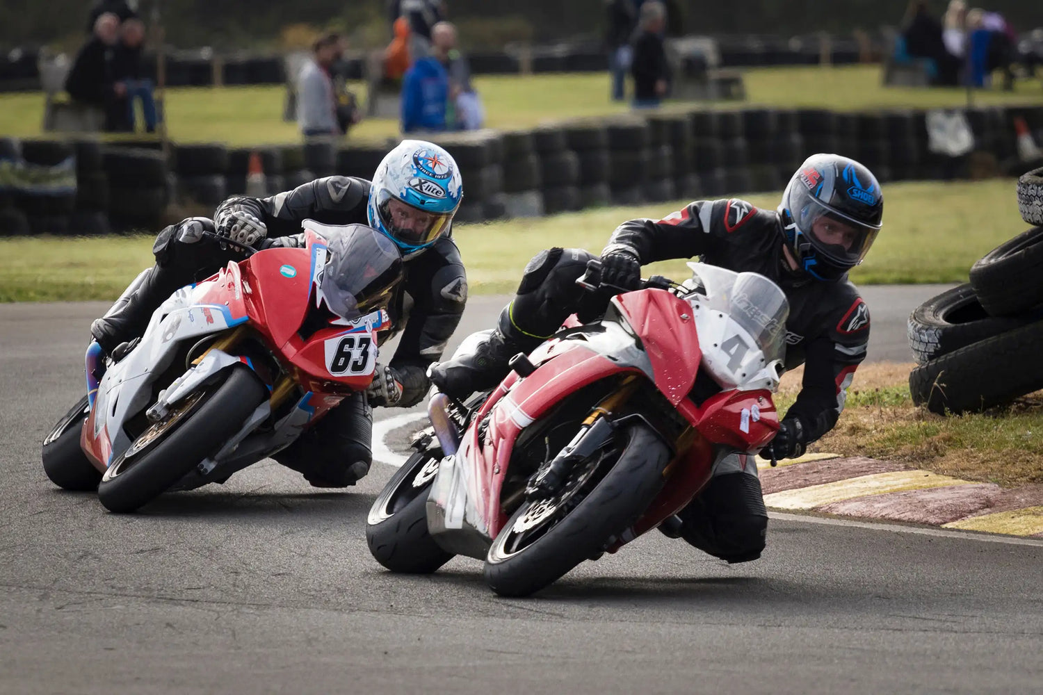 Two motorcyclists racing on a track with helmets and racing gear.