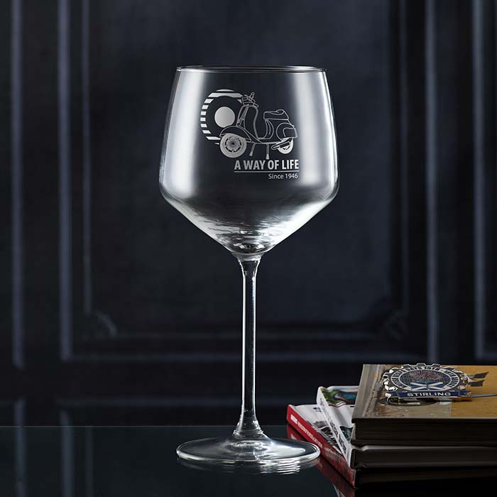 Gin  glass with engraved scooter design and text on a dark background