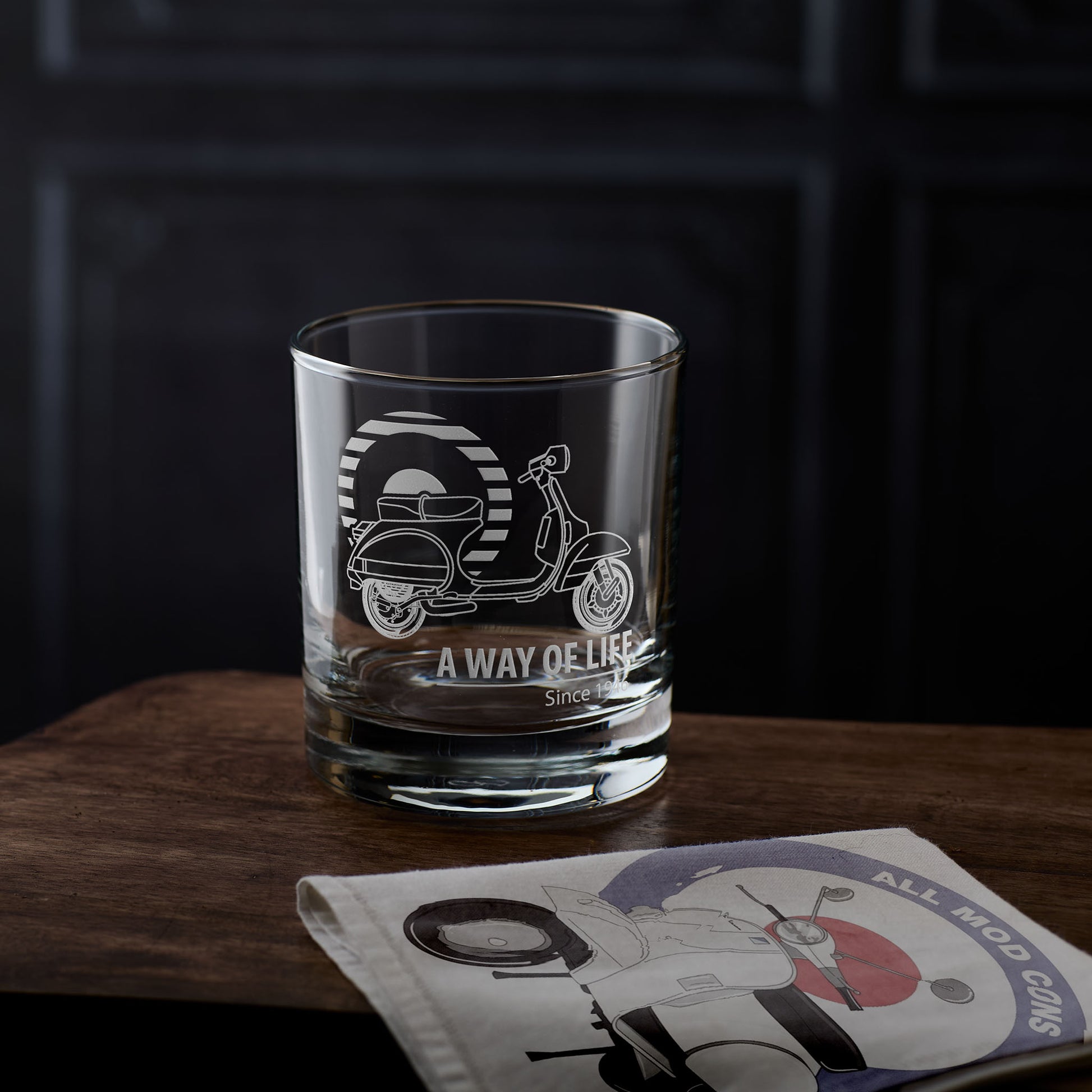 Clear whisky glass with scooter design and text on a wooden surface