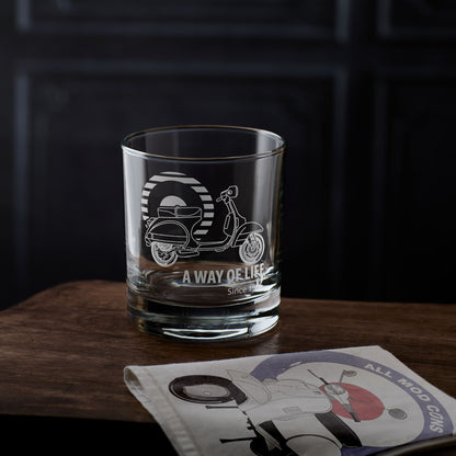 Clear whisky glass with scooter design and text on a wooden surface