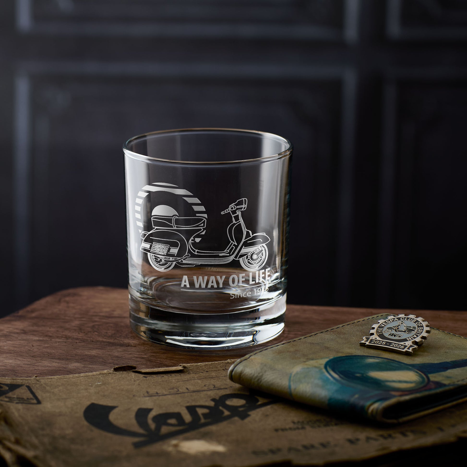 Vespa whisky glass with a Rally 200 scooter engraving on a wooden surface with a dark background