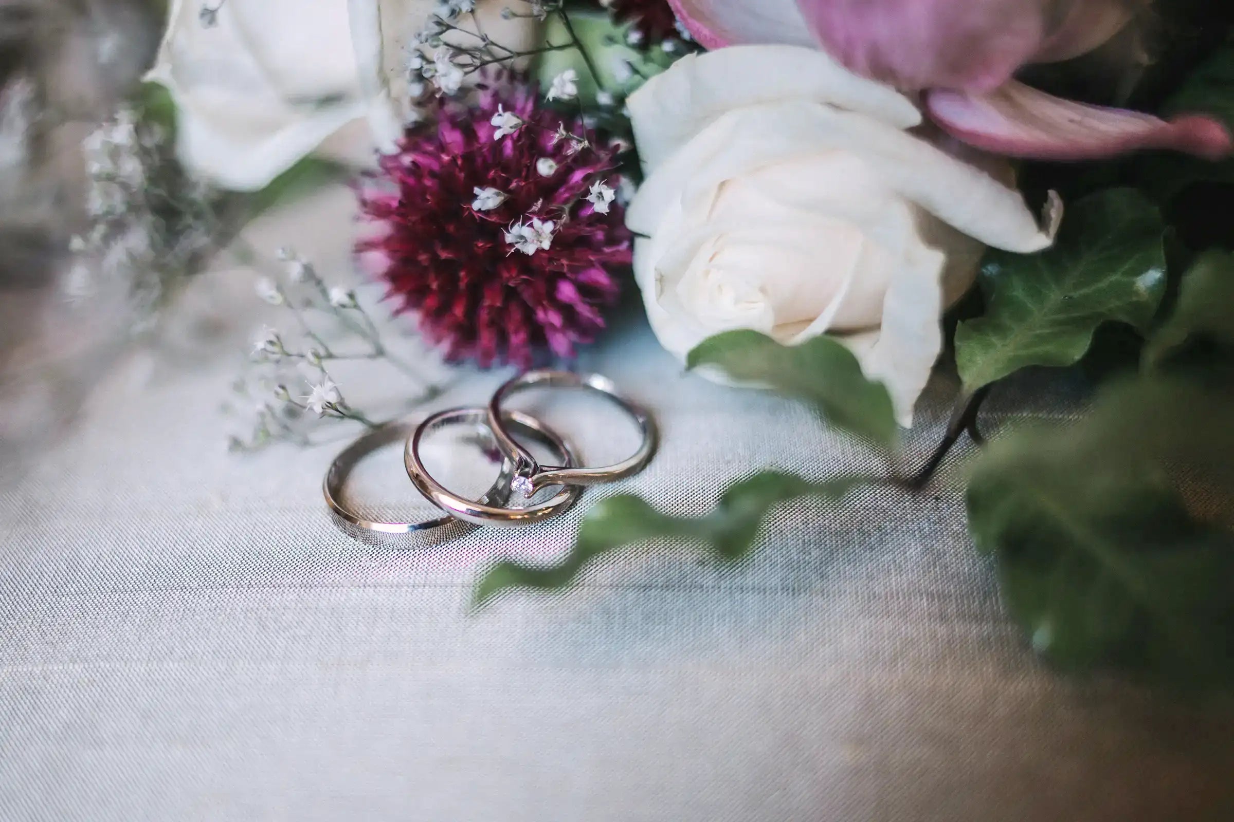 Two wedding rings on a tablecloth with flowers in the background